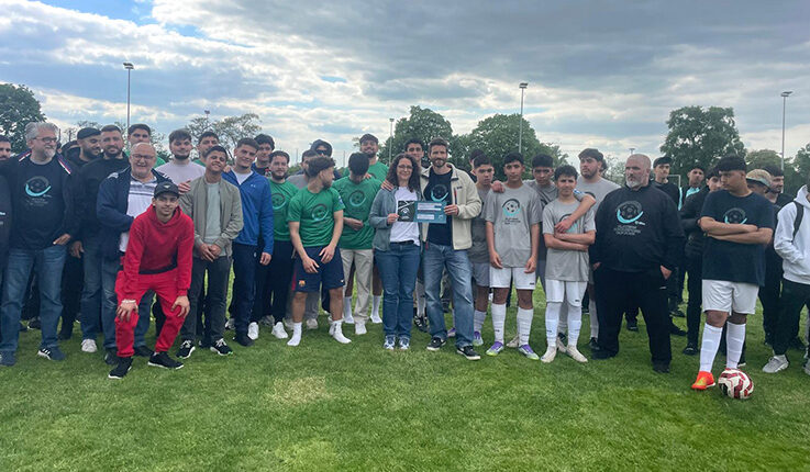 Eine große Gruppe, darunter Fußballspieler in Sportkleidung und andere in Freizeitkleidung, posieren nach dem Players for Purpose Cup gemeinsam auf einer Wiese. Einige Spieler halten eine Urkunde und einen Pokal für den 6. Platz und ein Preisgeld von 750 Euro in der Hand.